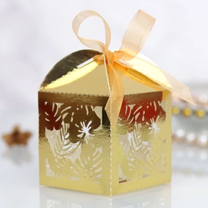 Detailed laser-cut hibiscus and tropical leaf patterns on a gold candy gift box with ribbon
