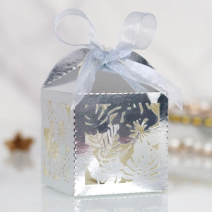Macro view of silver laser-cut tropical leaf patterns and silk ribbon on gift box