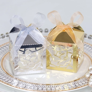 Detail of laser-cut rose wedding favor boxes in gold and silver with organza ribbon bows