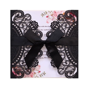 Macro shot of glittery black laser-cut invitation with satin bow and floral inner card