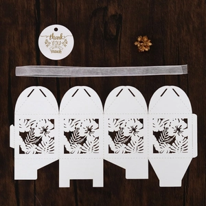 Flat lay of white laser-cut wedding favor box with tropical leaf pattern and ribbon