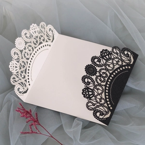 Detail of cream laser-cut wedding invitation with black glitter lace and floral lace edge