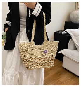 Close-up of woven straw tote bag with brown wavy lines and purple floral pendant detail