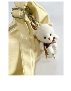 Detail view of beige crocodile embossed leather bag with white plush bear charm