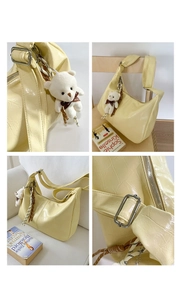 Detail view of pale yellow crescent crossbody bag with crocodile texture and bear charm