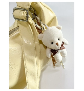 Close-up of creamy yellow crocodile texture bag with silver buckle and plush bear charm