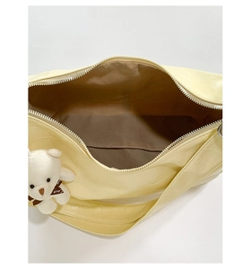 Detail view of large yellow croissant bag with croc pattern and plush bear charm