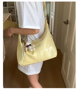 Detail of pale yellow hobo bag featuring crocodile pattern leather and a cute bear charm