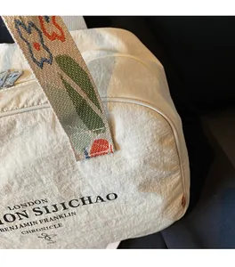 Close-up of off-white nylon travel bag with floral embroidered strap and zipper detail