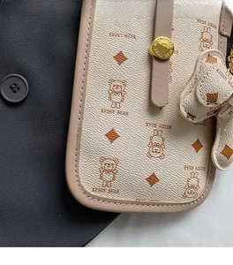 Close-up of beige leather shoulder bag with bear pattern and a teddy bear charm