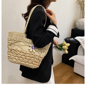 Detail of hand-woven straw tote bag featuring a purple floral charm and natural textures