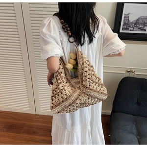 Detail of woven straw tote bag with chunky dark brown wooden bead shoulder strap accent