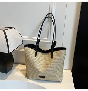 Close-up of woven straw tote bag with black leather trim and knotted strap details