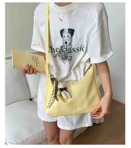 Detail of yellow crocodile embossed crossbody bag with bear charm on a female model