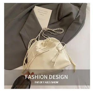 Detail showing creamy white bucket bag with drawstring bow and chain strap on grey blazer