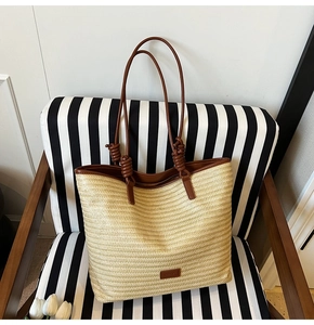 Close-up of straw woven tote bag featuring deep brown leather handles with knot detail