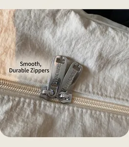 Detail of silver dual metal zippers on beige nylon fabric bag with engraved logo