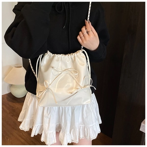 Detail of cream glossy leather backpack featuring three decorative bows and chain strap