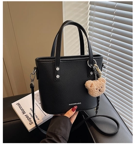 Close-up of black litchi pattern bucket bag with bear charm and adjustable strap