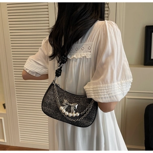Detail of black tweed shoulder bag with silver bow, pearls and knot strap on a model