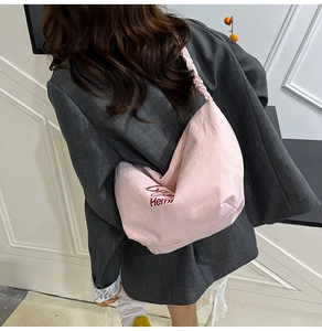 Pink canvas hobo bag with pleated shoulder strap and red embroidery detail worn by model