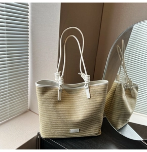 Detail of woven straw tote bag with knotted handles and metallic brand logo