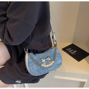 Detail of light blue denim crescent bag with silver bow, pearls and metal chain