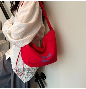 Detail of red pleated canvas hobo bag with blue brand embroidery on the shoulder strap