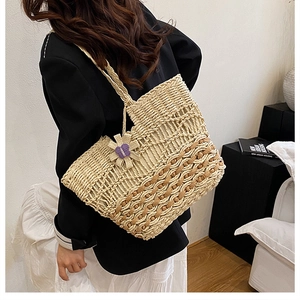 Detail of hand-woven straw tote with purple flower charm on model's shoulder