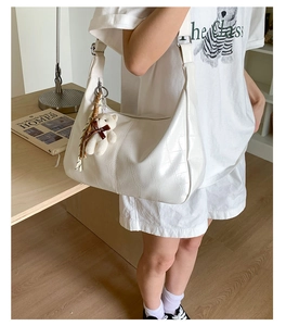 White croissant bag with crocodile pattern and bear pendant shown on model