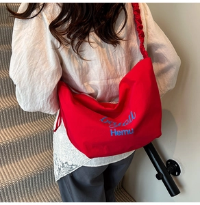 Detail of red canvas tote bag showing ruched shoulder strap and blue brand embroidery