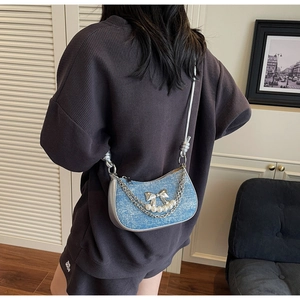Detail of blue denim underarm bag featuring a silver bow and elegant pearl chain accent