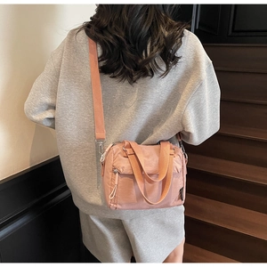 Rear view of a model wearing a pink nylon crossbody bag on a wooden staircase