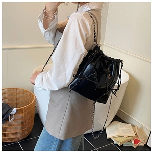 Detail of black drawstring bucket bag with bow and silver chain strap on model