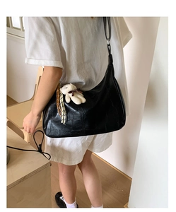 Detail of black faux crocodile leather hobo bag with teddy charm and braided strap