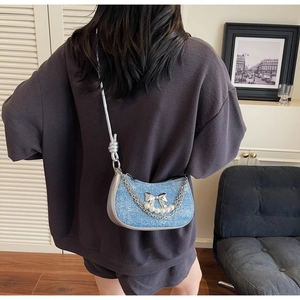 Model wearing a light blue denim hobo bag with a silver bow and elegant pearl chain detail