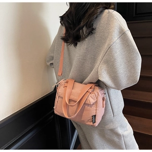 Close-up of pink nylon crossbody bag with adjustable strap and brand tag on a model