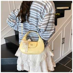 Close-up of yellow crescent pleated handbag with a delicate pearl bow charm and logo