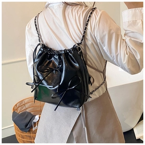 Detail of black drawstring bucket bag with decorative bows and metallic chain straps