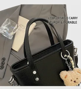 Detail of black lychee grain leather handbag with silver rivets and cute bear pendant