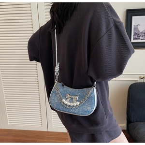 Detail of blue denim underarm bag with silver bow, pearls, and chain decorations