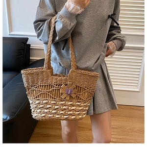 Straw tote bag with purple butterfly charm worn on shoulder by model in home setting
