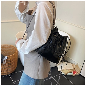 Detail view of black leather drawstring bucket bag with silver chain and bow accent