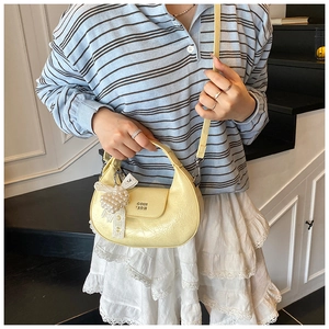 Pale yellow crescent bag with pearl bow detail shown worn by a model in a casual setting
