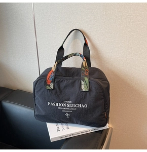 Detail of black nylon tote bag featuring colorful floral woven handles and white art prints
