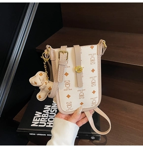 Detail of a creamy white cartoon bear crossbody bag with golden hardware and bear charm