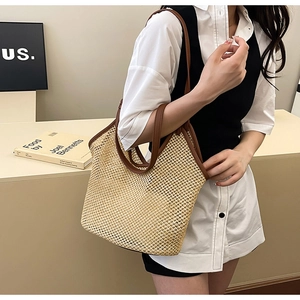 Détail du sac cabas en paille tissée avec anses en cuir marron porté par un mannequin