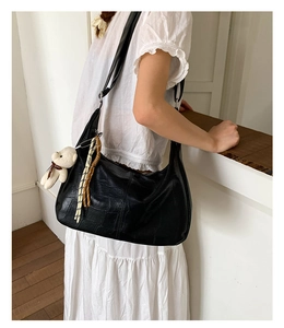Detail of black crocodile texture hobo bag with plush bear charm and woven tassel
