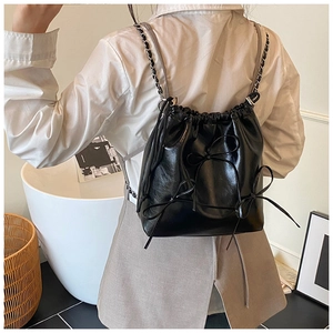 Detail of a black drawstring bucket backpack with bows and silver chain straps on a model