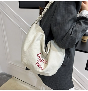 Detail of off-white canvas tote bag featuring a red logo and unique scrunchie strap design